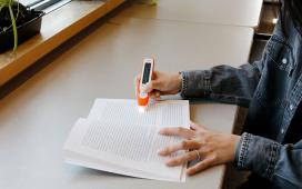 Close up of hands using a C-Pen device to highlight words in a book which it reads aloud.