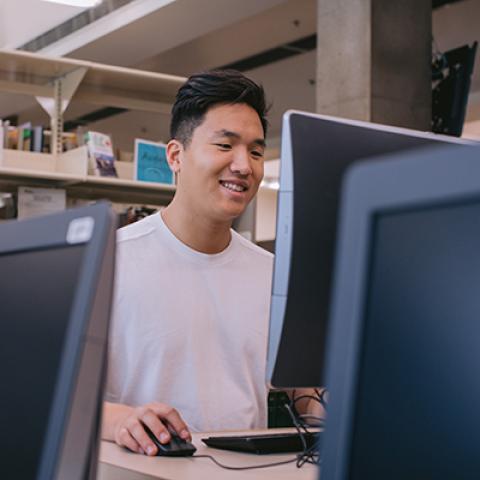 Young man with dark hair wearing white t-shirt looks at computer screen.