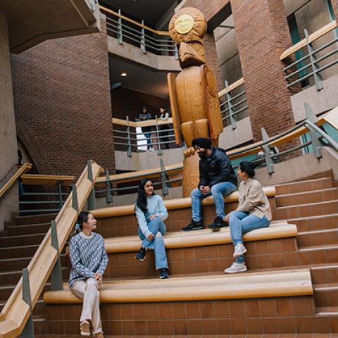 Four young people sit on steps below carved wooden Welcome Post.