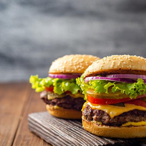Two hamburgers on a wooden cutting board.