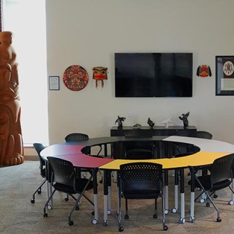 Room with Indigenous post in left corner and circular table divided into red, yellow, white and black sections.