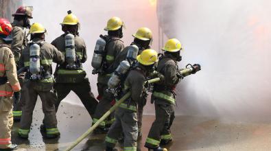 Group of firefighting students fighting fire while instructors look on.