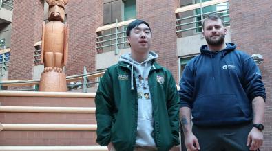 Two male students in atrium at JIBC's New Westminster campus, with Welcome Post in the background.