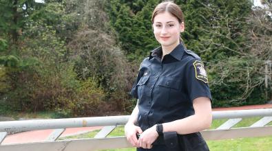 Woman in BC Corrections officer uniform standing at overlooking JIBC courtyard with hands resting on utility belt.