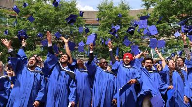 JIBC graduates in blue gowns toss their blue grad caps in the air.