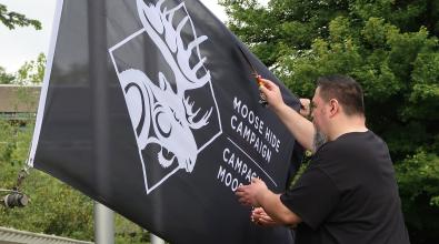 Man waves feather over a black flag with an image of a moose that says, "Moose Hide Campaign"