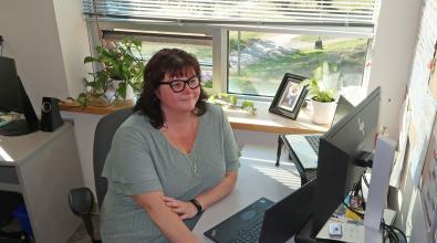 Woman wearing glasses sitting at a desk with hand on mouse looking at computer monitor.