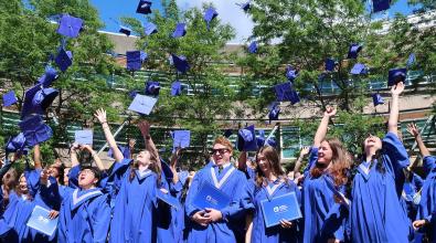 JIBC graduates in blue convocation gowns toss their caps in the air.