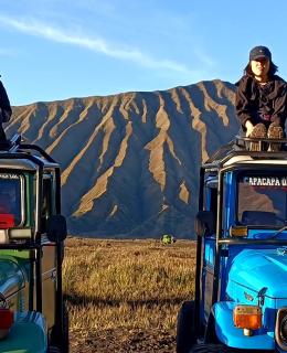 Four students sit atop jeeps with Indonesian mountains in background.