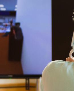 Man wearing virtual reality headset seen facing video screen showing VR simulator. 