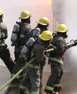 Group of firefighting students fighting fire while instructors look on.