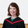 Woman with dark hair wearing black graduation gown with red trim.