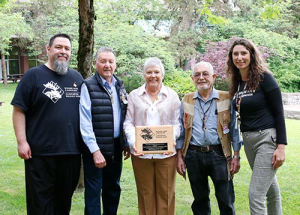 Three men and a woman pose with a plaque held by a second woman in the centre.