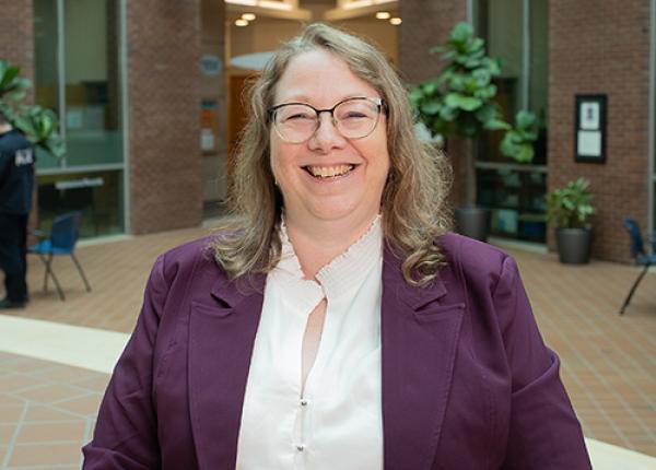 Woman with glasses wearing dark purple jacket and white blouse.
