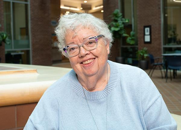 Grey-haired woman wearing glasses and light blue sweater.