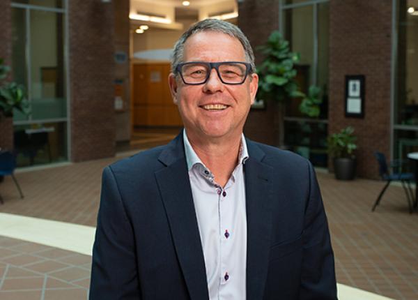 Man wearing glasses, dark jacket and light buttoned shirt.
