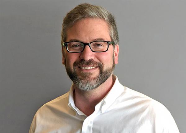 Man with beard wearing glasses and a white shirt.