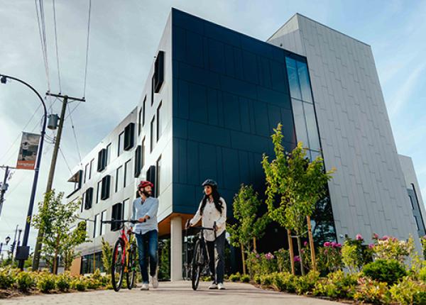 Two people walking bicycles in front of building.